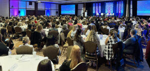 Group of pople sitting around tables looking at a speaker at the front of the room